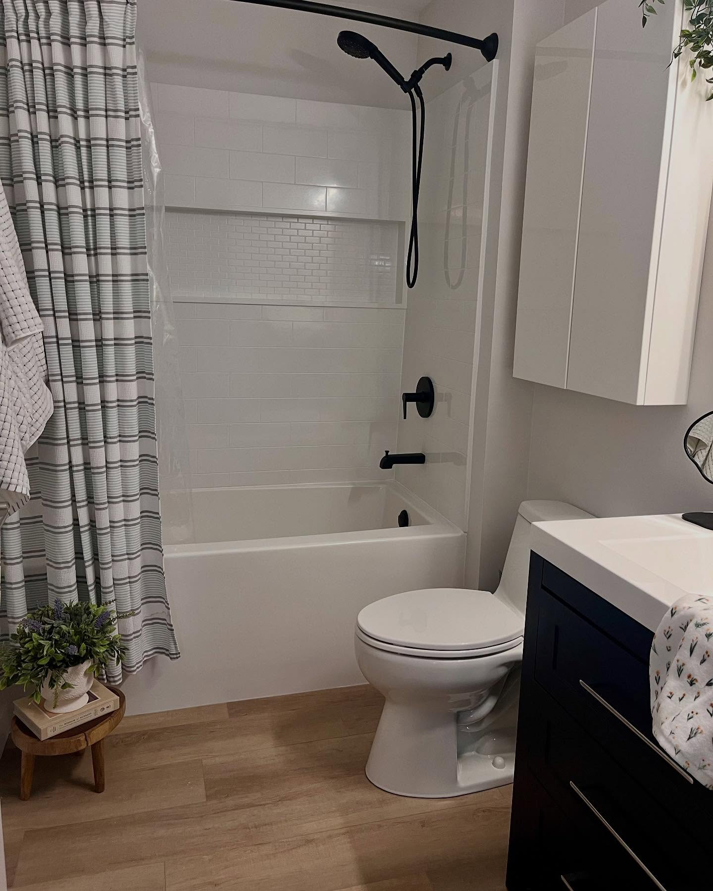 Finished Project Lotus bathroom with white subway tile, a long shower niche, matte black fixtures, and wood-look flooring