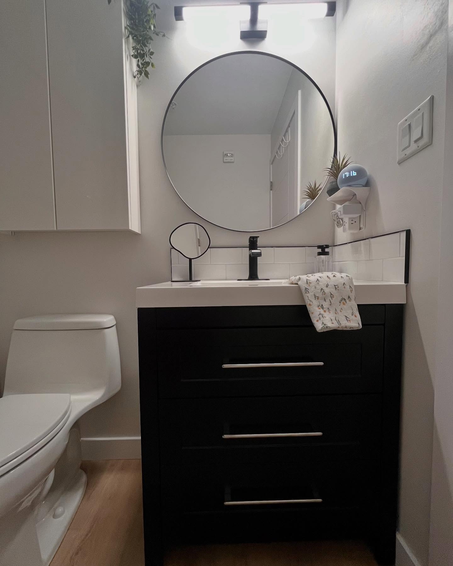 Finished Project Lotus vanity with a navy drawer bank, white integrated sink, round black mirror, and matte black faucet