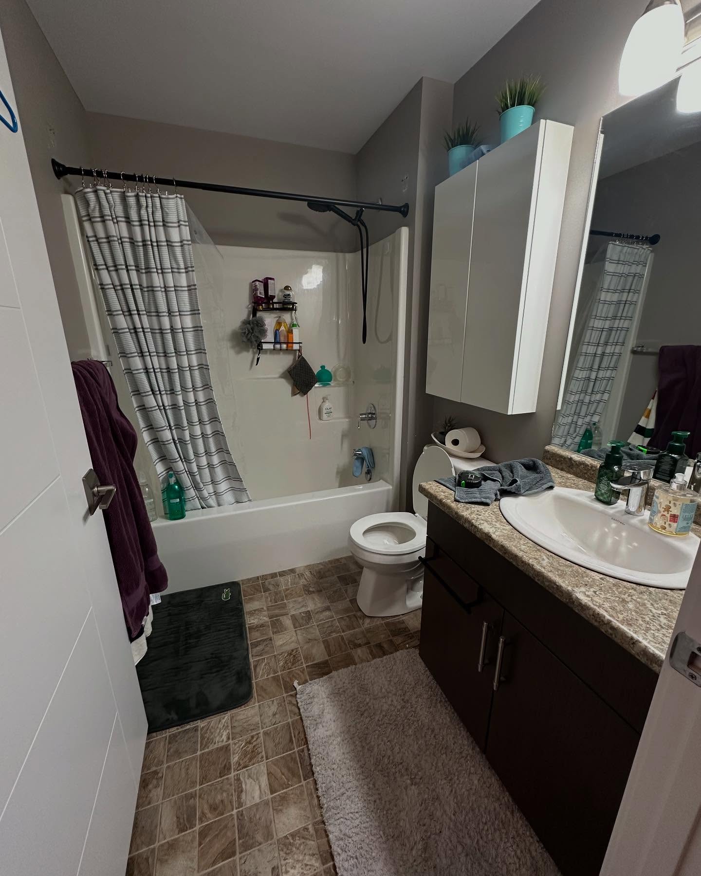 Project Lotus bathroom before renovation, with a dark wood vanity, speckled counter, grey walls, and tan floor tile