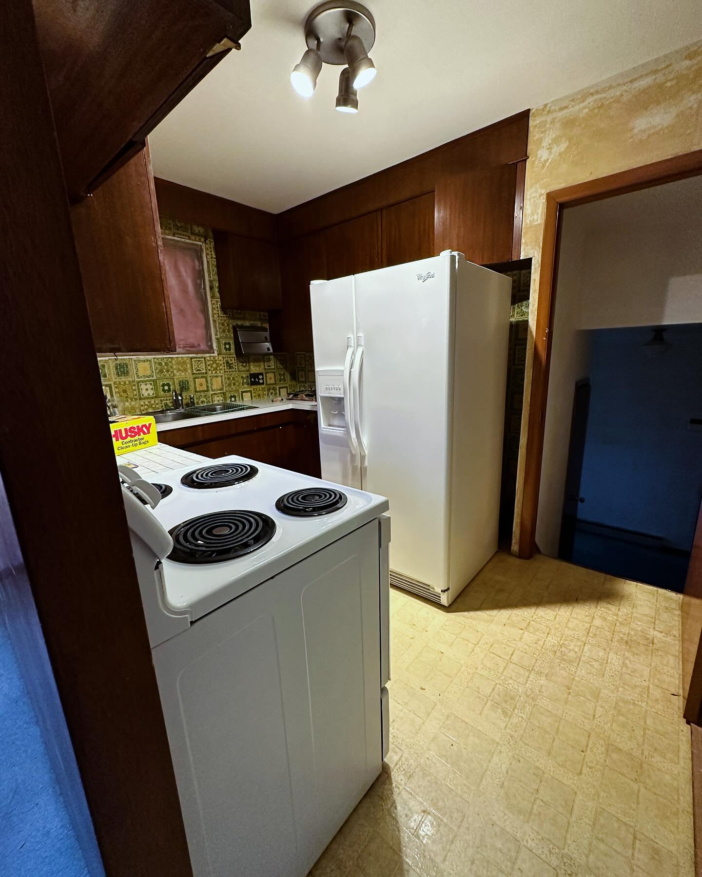 Project Rose kitchen before renovation, with dark wood cabinets, green patterned tile, a white coil-top range, and a white refrigerator