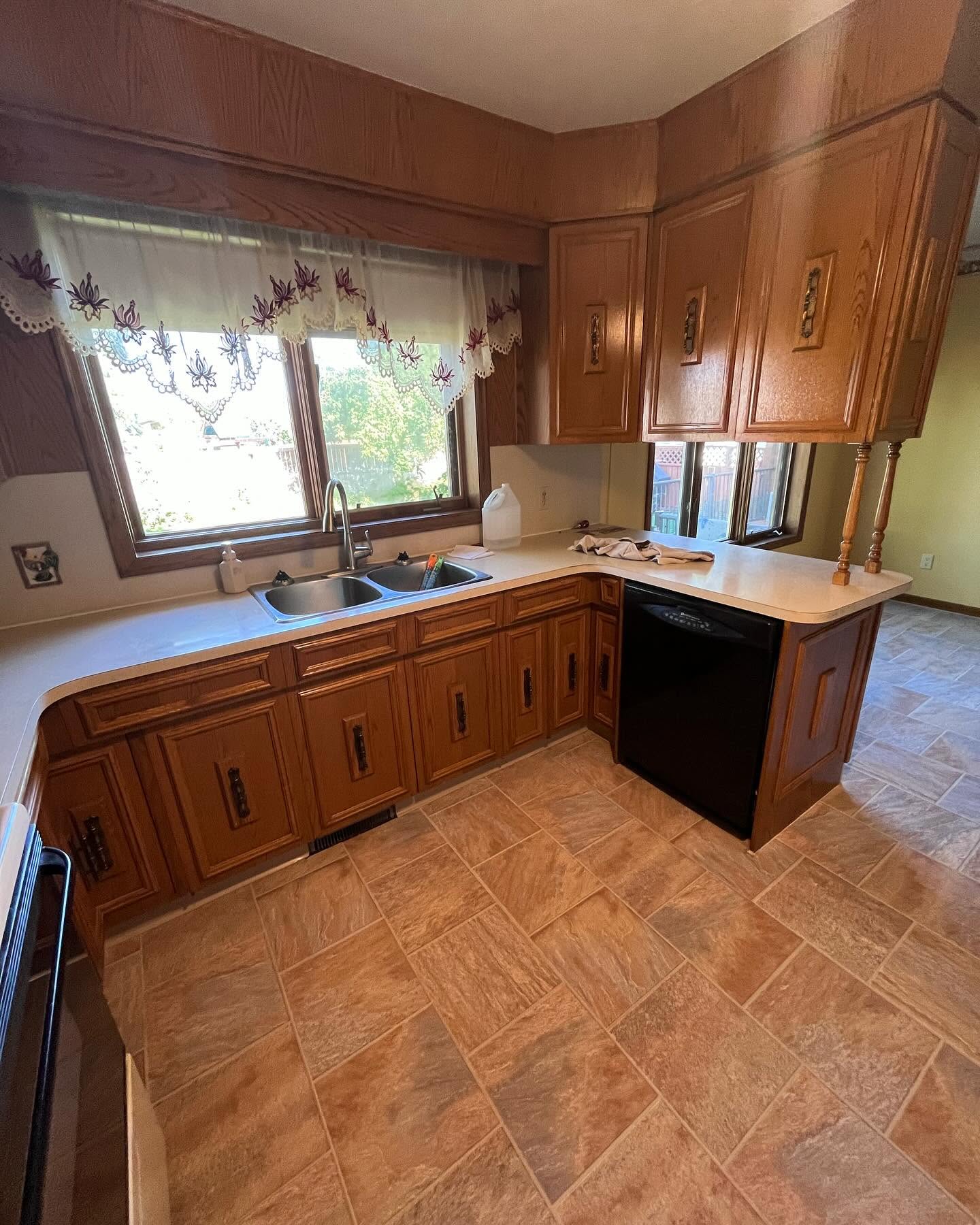 Wider view of the oak Project Hydrangea kitchen before renovation, with a peninsula sink and hanging cabinets